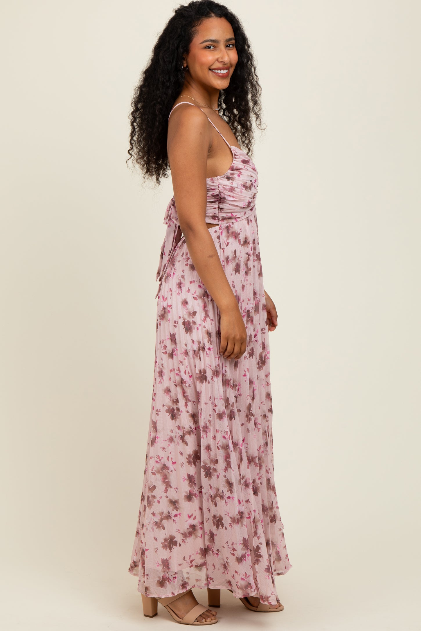 woman wearing a light pink floral maxi dress with spaghetti straps and gathered detailing, standing sideways