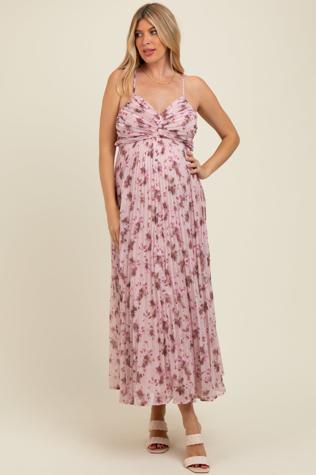 woman wearing a pink floral maternity maxi dress with a twist front detail and spaghetti straps