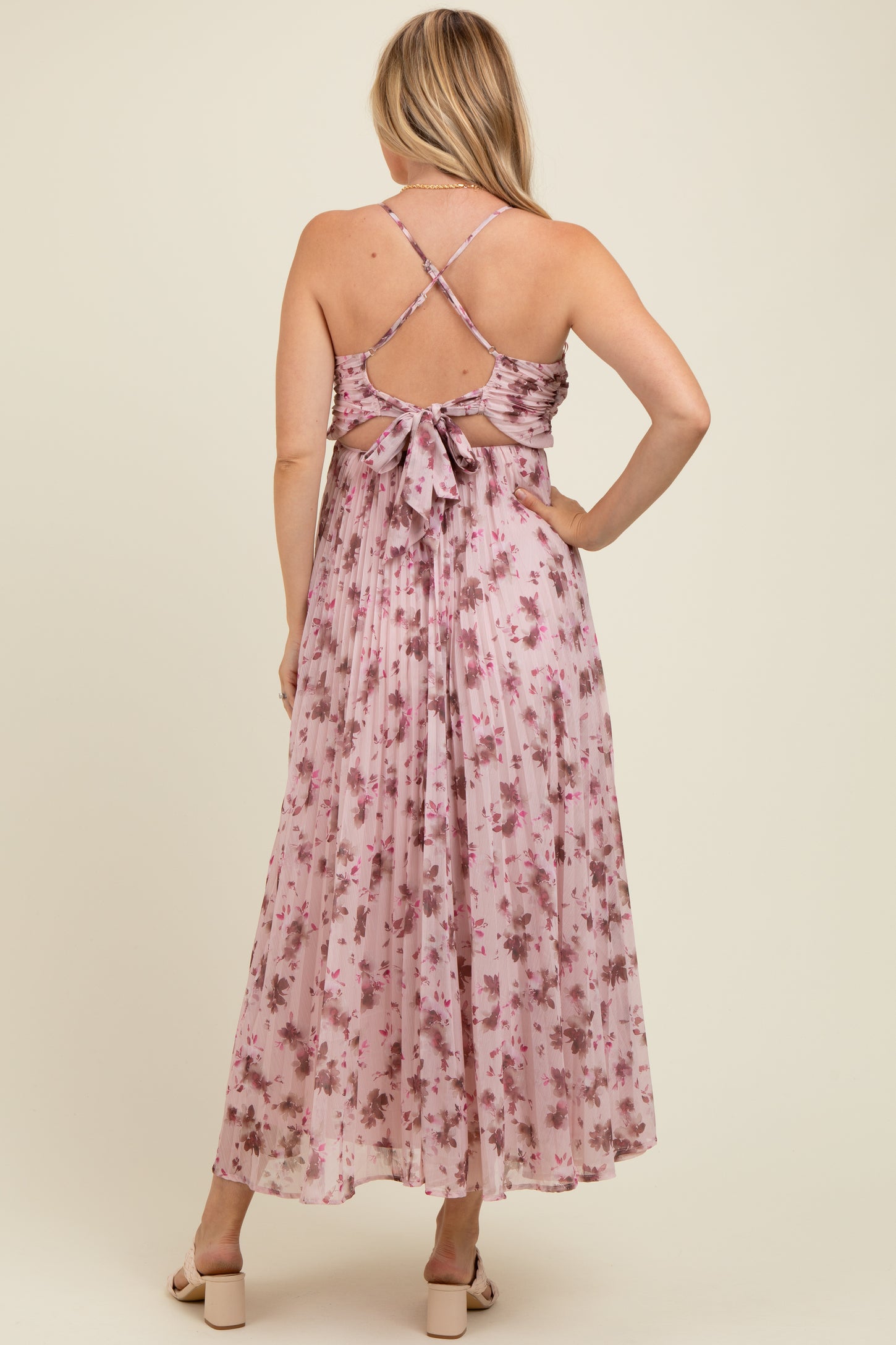 woman wearing a pink floral maternity maxi dress with a crisscross back detail and bow accent