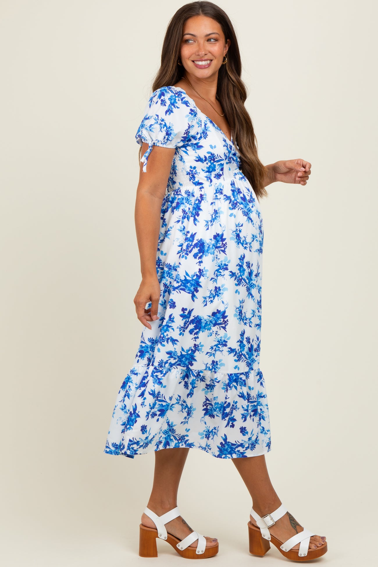 woman wearing a blue and white floral maternity dress with short sleeves and a tiered hem, showing her baby bump