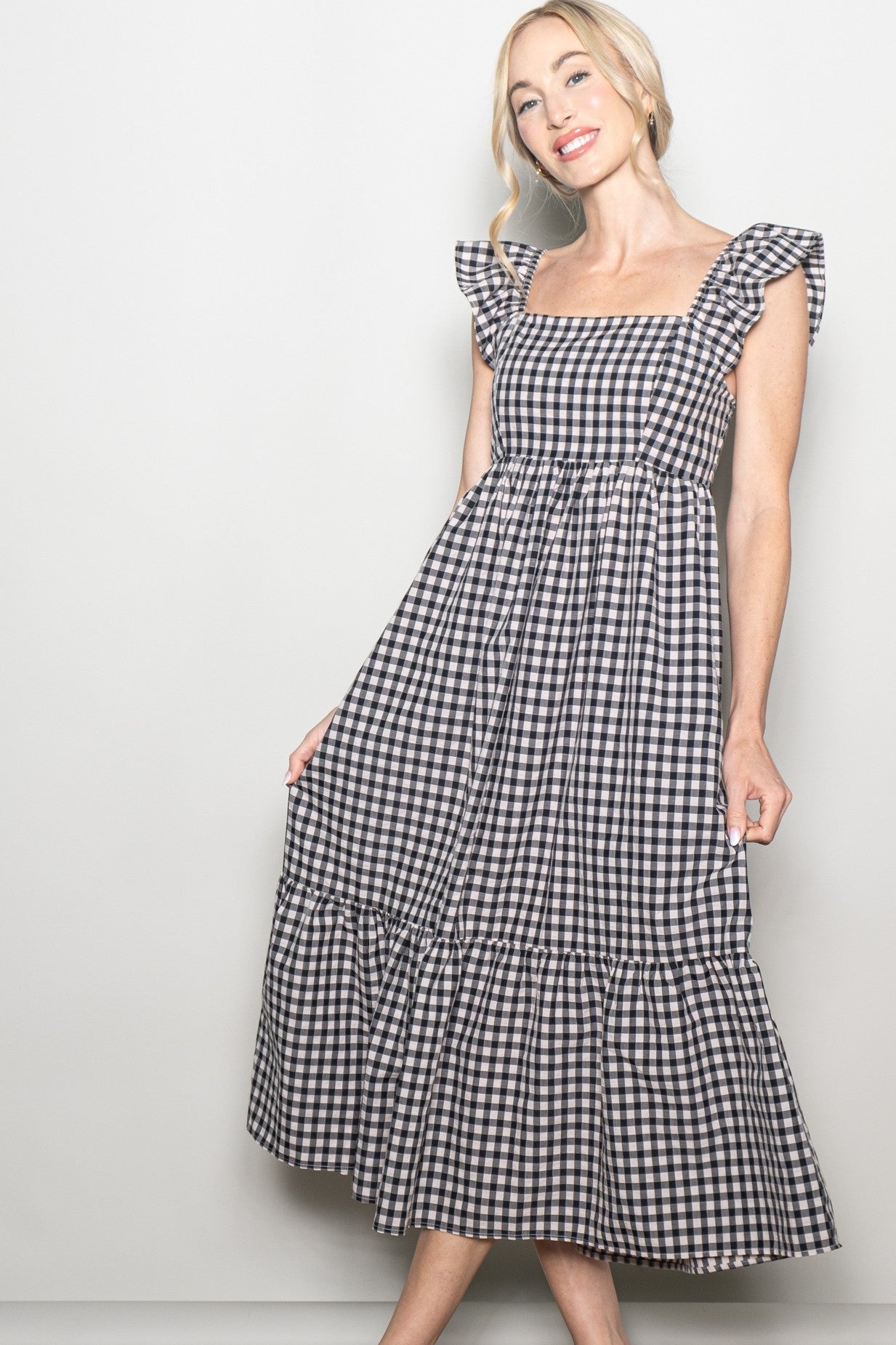 woman wearing a black and white gingham print midi dress with ruffled sleeves and a tiered hem