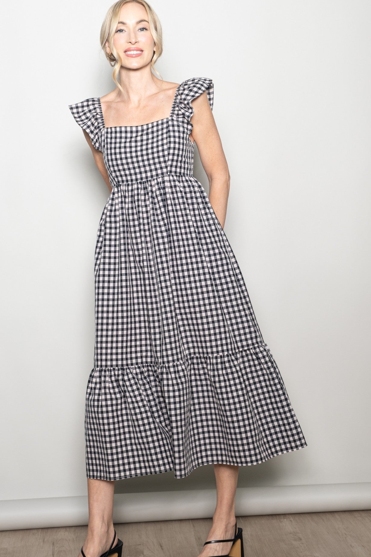 woman wearing a black and white gingham midi dress with ruffle sleeves and a tiered skirt