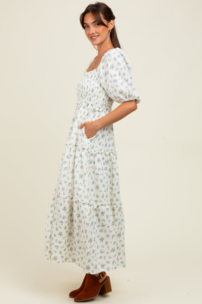 woman wearing a white floral maxi dress with puff sleeves and pockets, standing in profile with brown ankle boots