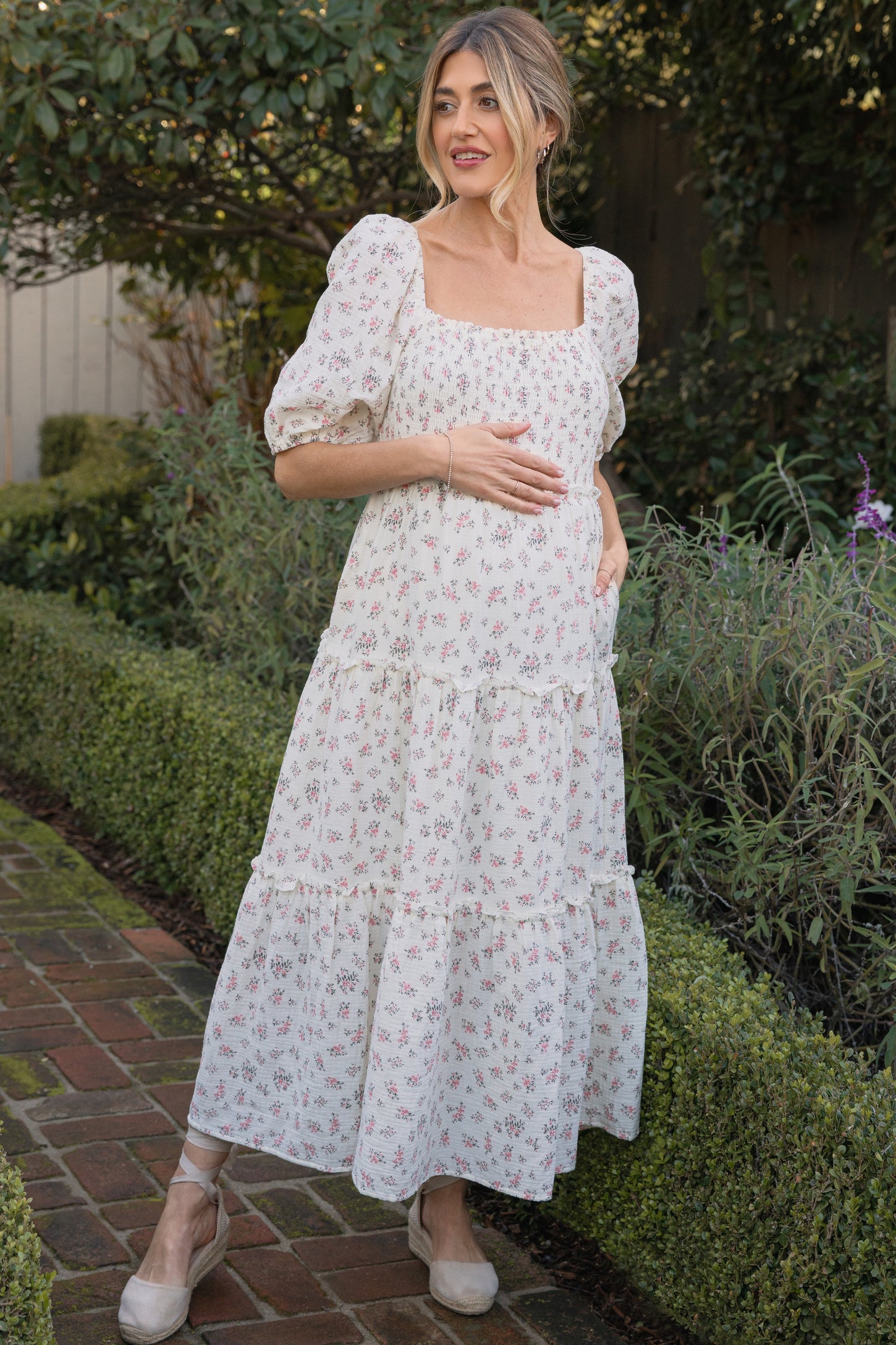 woman wearing a white floral maternity dress with puff sleeves and a tiered skirt, showing her baby bump