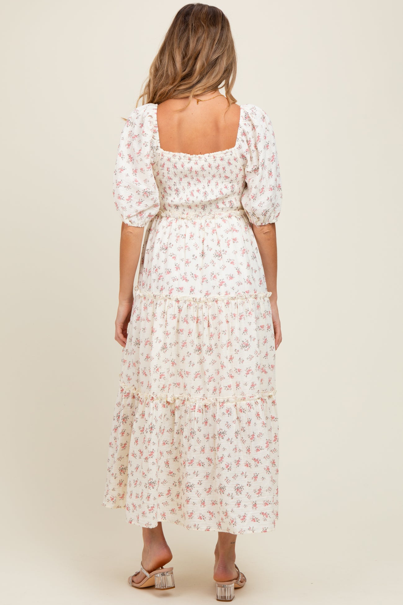 woman wearing a white floral print maternity dress with puff sleeves and a tiered skirt, showing her baby bump