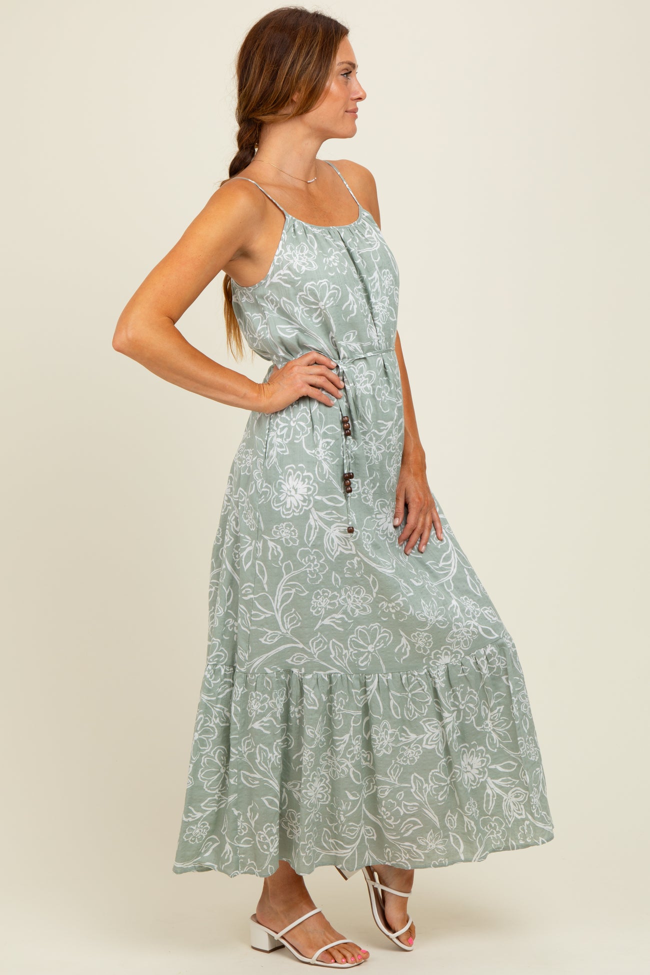 woman wearing a light green floral maxi dress with spaghetti straps and a tiered skirt, standing sideways