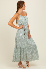 woman wearing a light green floral maxi dress with spaghetti straps and a tiered skirt, standing sideways