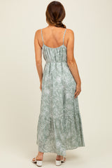 woman wearing a green floral maxi dress with thin straps and a tiered skirt, shown from the back