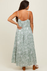 woman wearing a light green floral maternity maxi dress with a backless design and adjustable straps