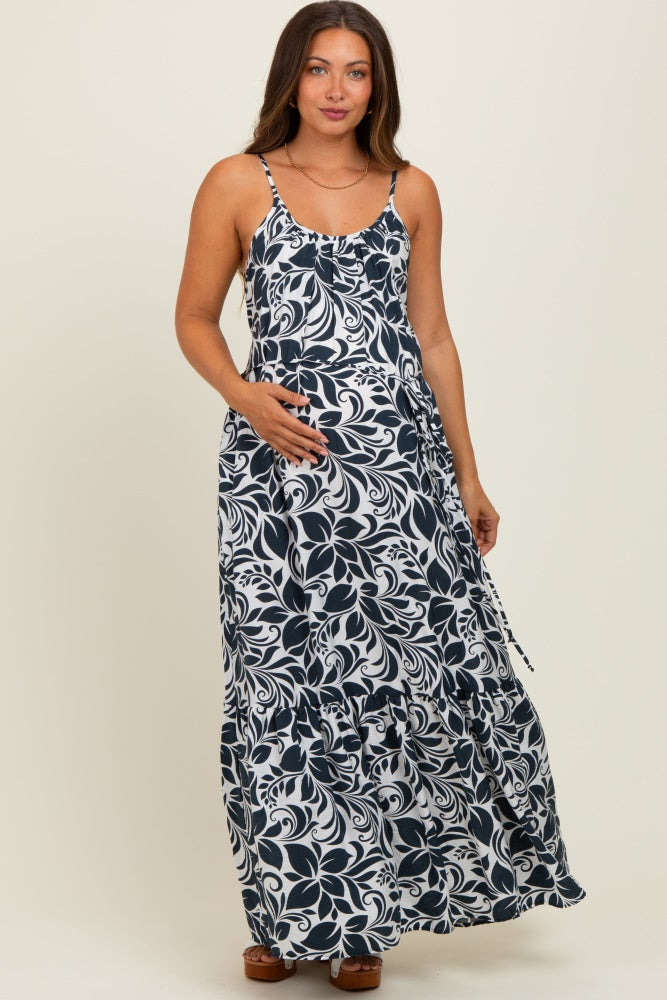 woman wearing a navy and white floral print maternity maxi dress with adjustable straps and a cinched waist, holding her baby bump