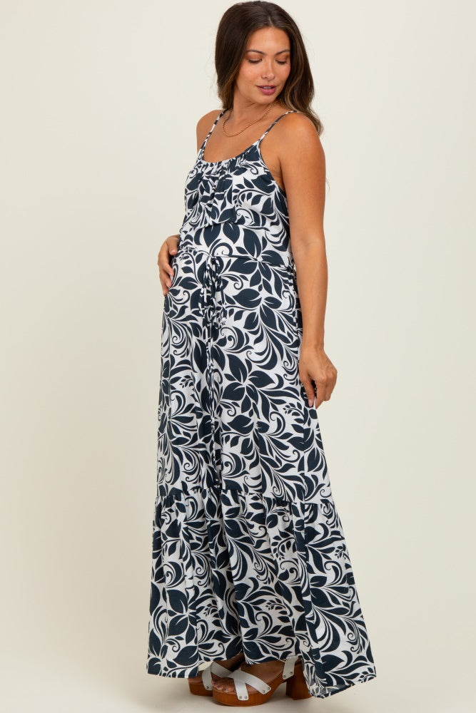 woman wearing a navy and white floral print maternity maxi dress with adjustable straps and a flowing skirt, showing her baby bump