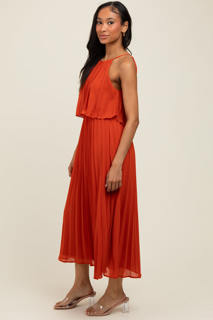 woman wearing an orange pleated sleeveless dress with a flowy silhouette and flat sandals
