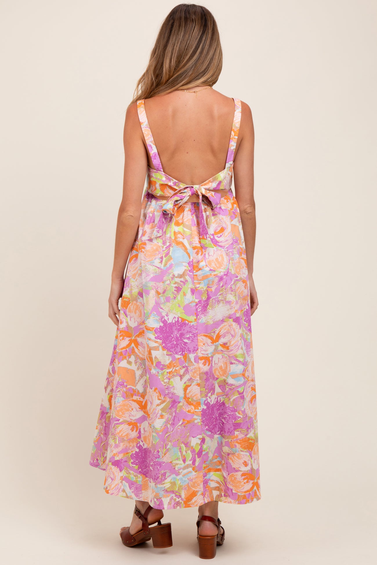 woman wearing a backless, floral print maternity maxi dress with a tied bow detail in the back