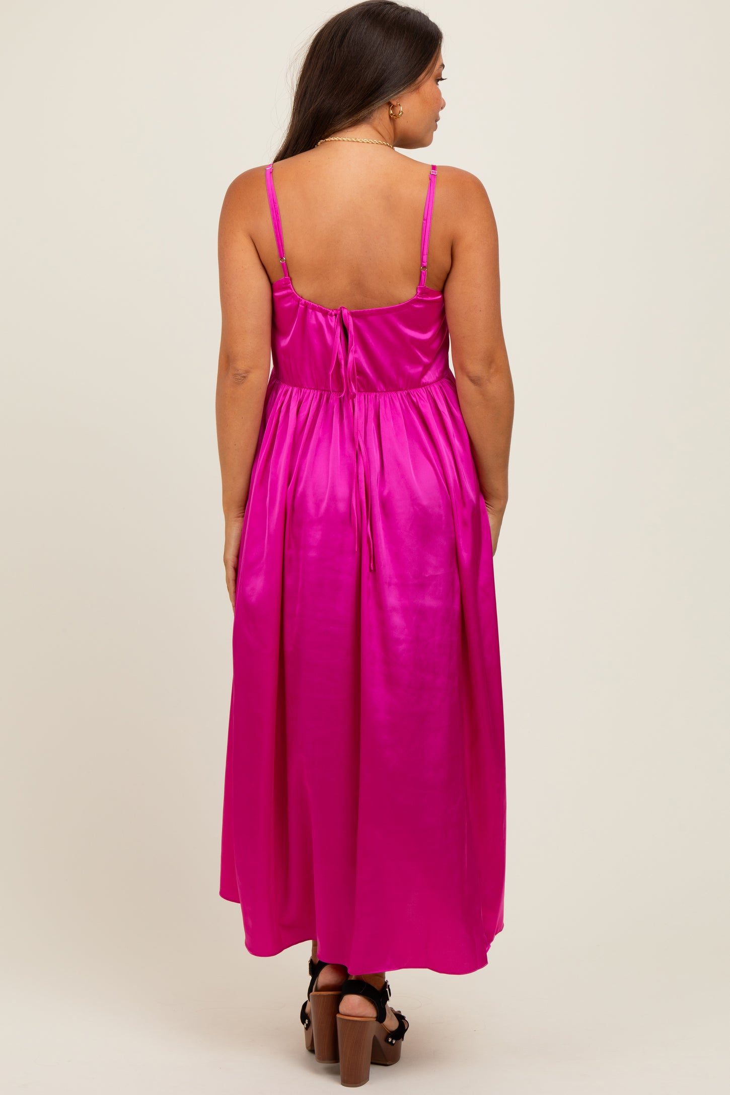 woman wearing a bright pink maternity maxi dress with a tied back detail and adjustable straps