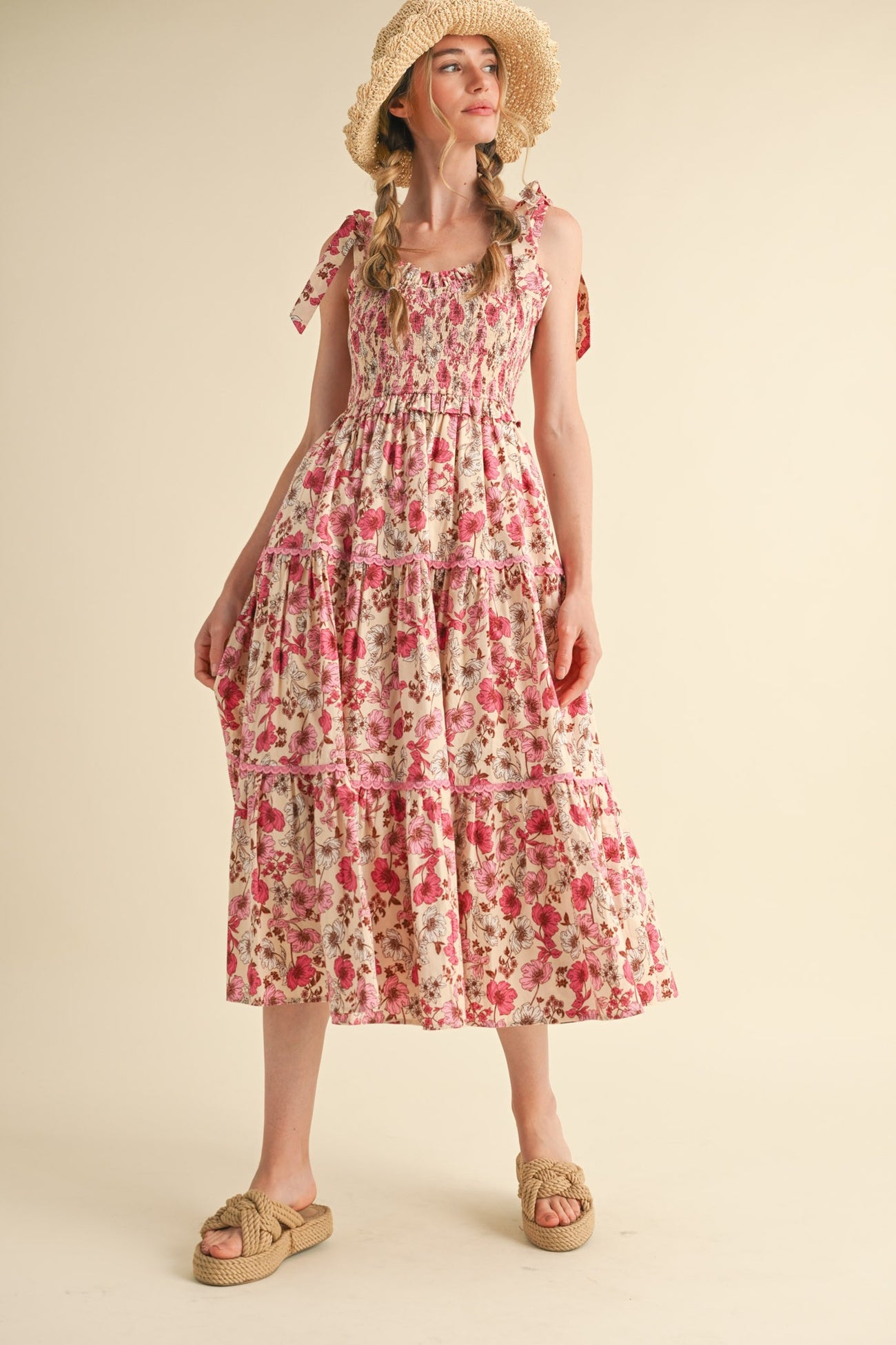 woman wearing a floral print maxi dress with tiered ruffles and bow straps, styled with a straw hat and sandals