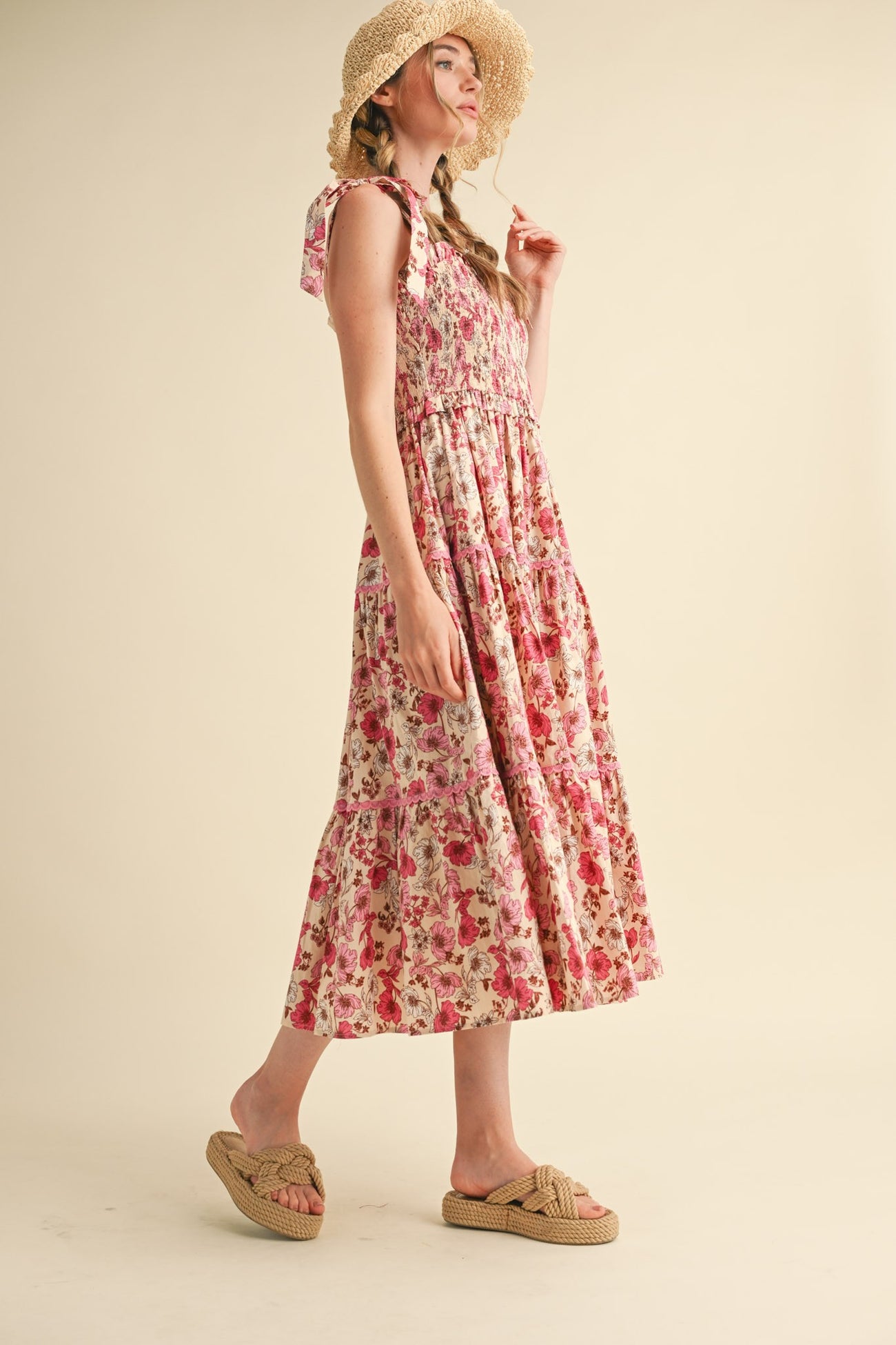 woman wearing a pink floral maxi dress with ruffled straps and a tiered skirt, paired with tan slide sandals and a straw hat