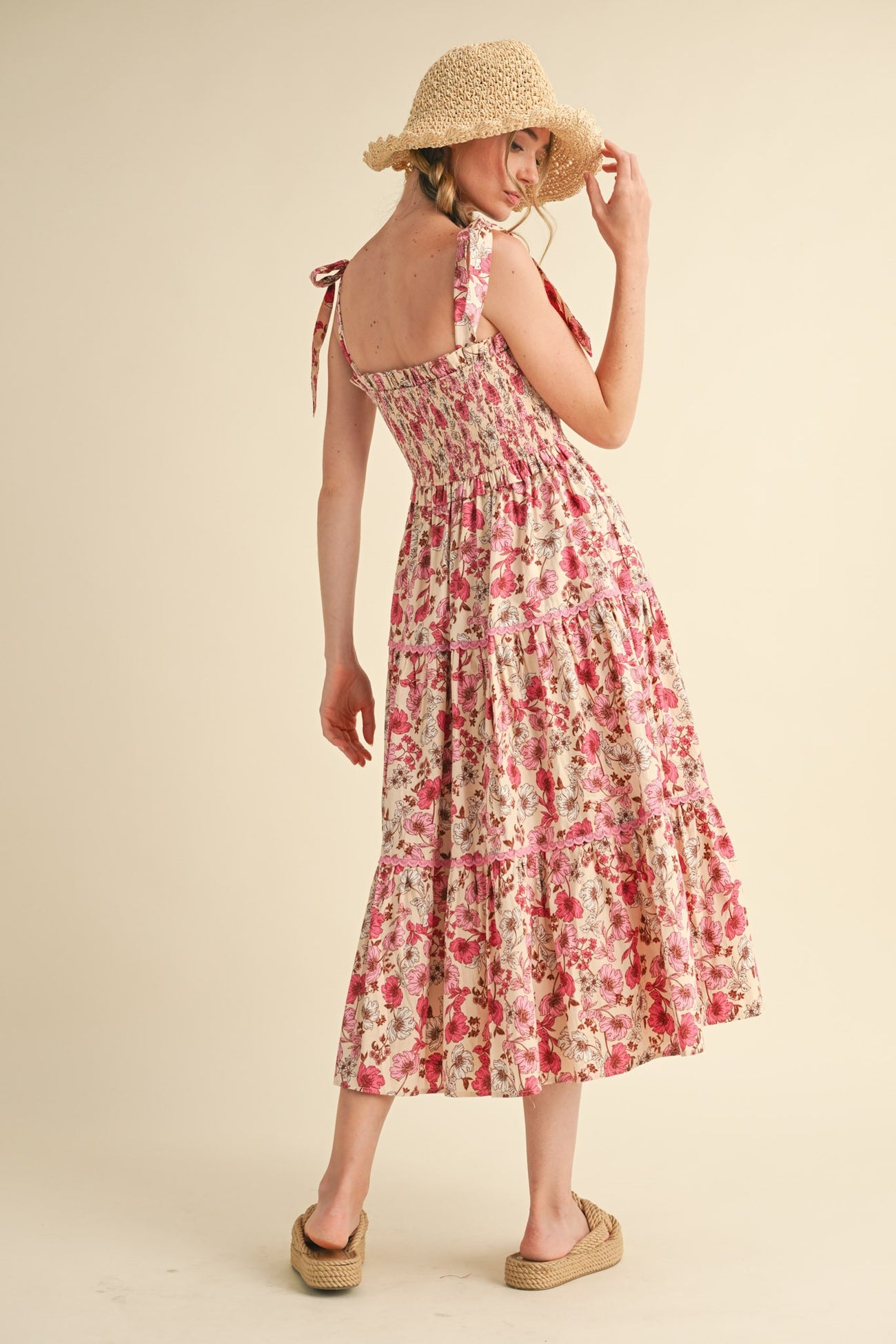 woman wearing a floral print midi dress with smocking and tie straps, paired with a straw hat and platform sandals
