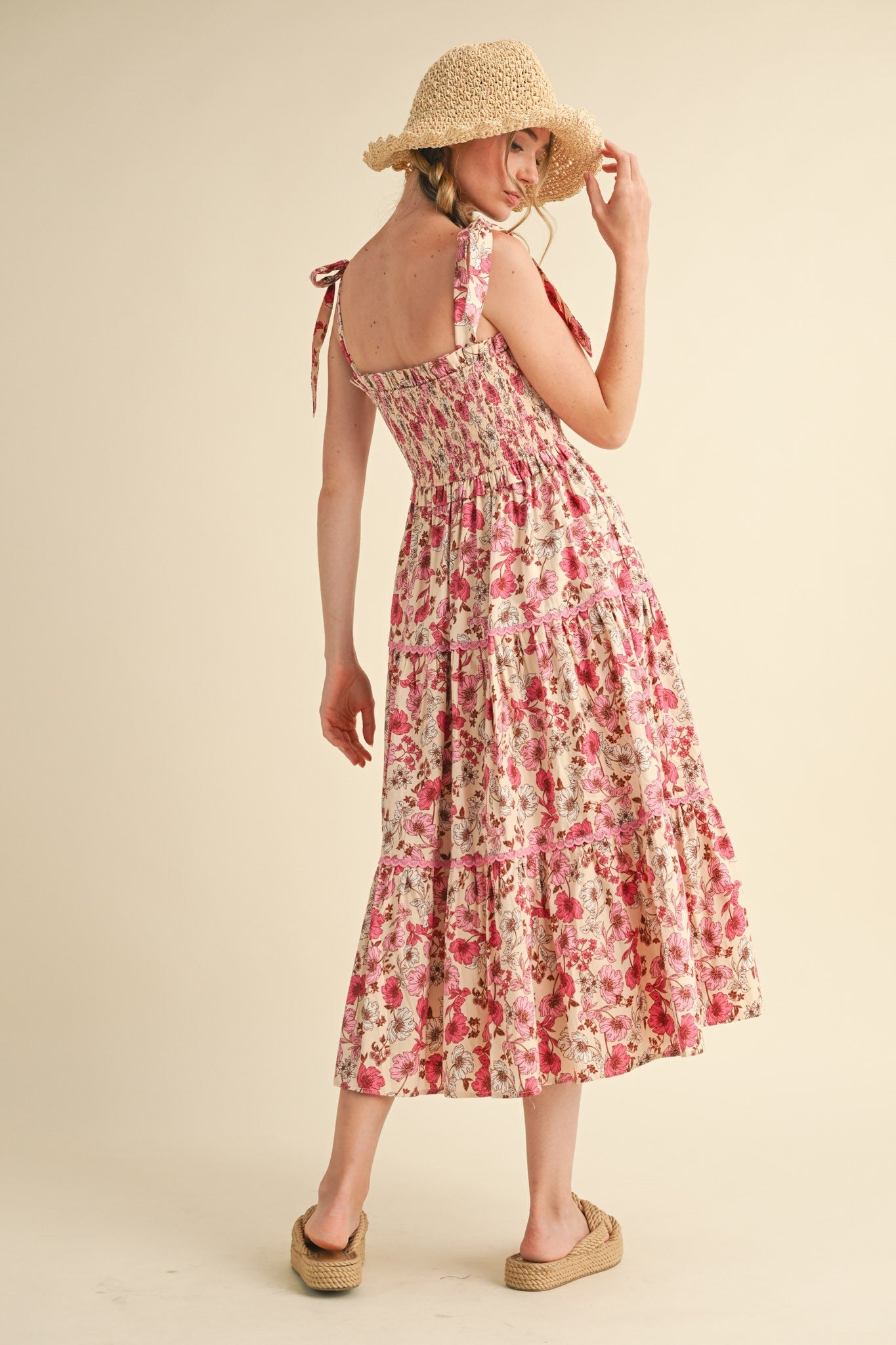 woman wearing a floral print midi dress with smocking and tie straps, paired with a straw hat and platform sandals