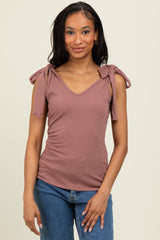 woman wearing a mauve ribbed top with v-neck and tie detailing on the shoulders, paired with blue jeans