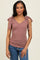 woman wearing a mauve ribbed top with v-neck and tie detailing on the shoulders, paired with blue jeans