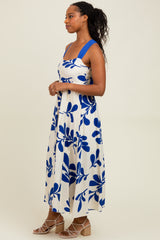 woman wearing a white maxi dress with blue leaf prints and wide straps, styled with wedge sandals