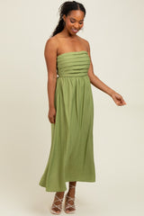 woman wearing a strapless olive green maxi dress with pleated bodice and flowing skirt
