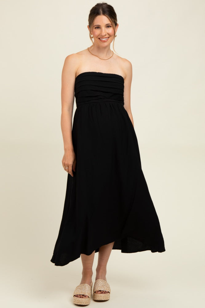 woman wearing a black strapless maternity dress with gathered bodice and flowy skirt, standing on a neutral background