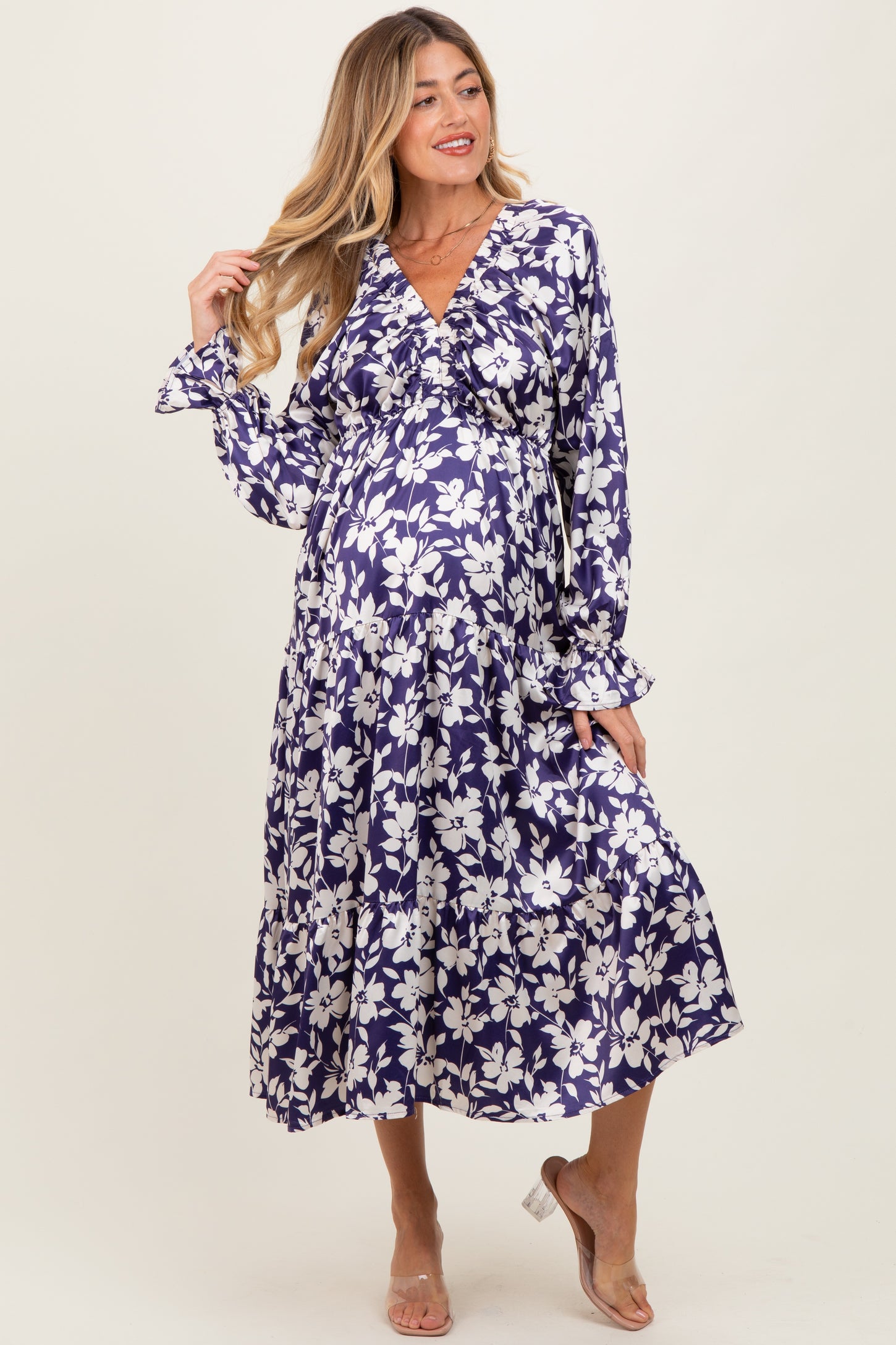 woman wearing a purple floral maternity dress with long sleeves and a flowy skirt, showcasing her baby bump