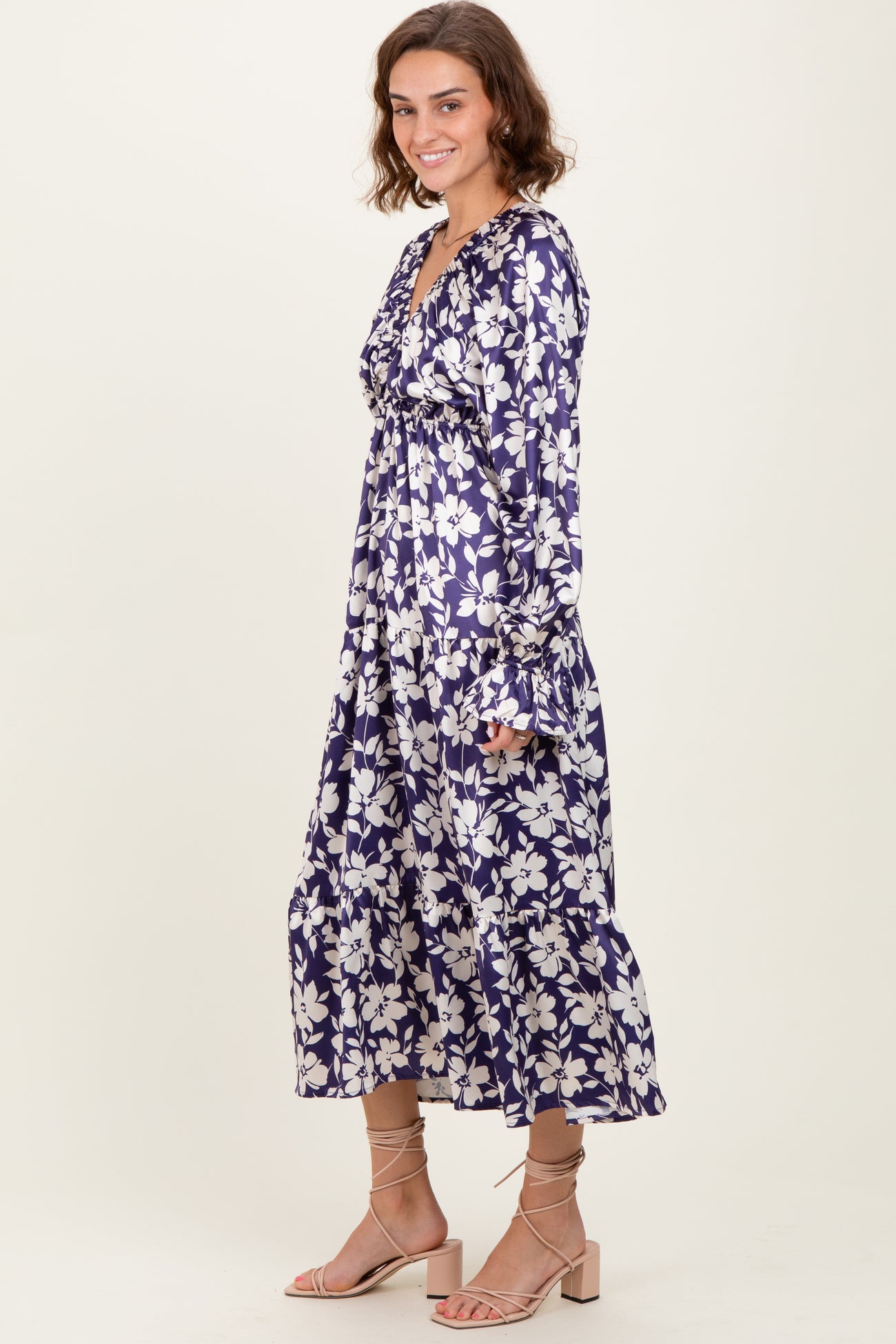 woman wearing a purple floral maxi dress with long sleeves and a v-neckline, standing elegantly against a neutral background