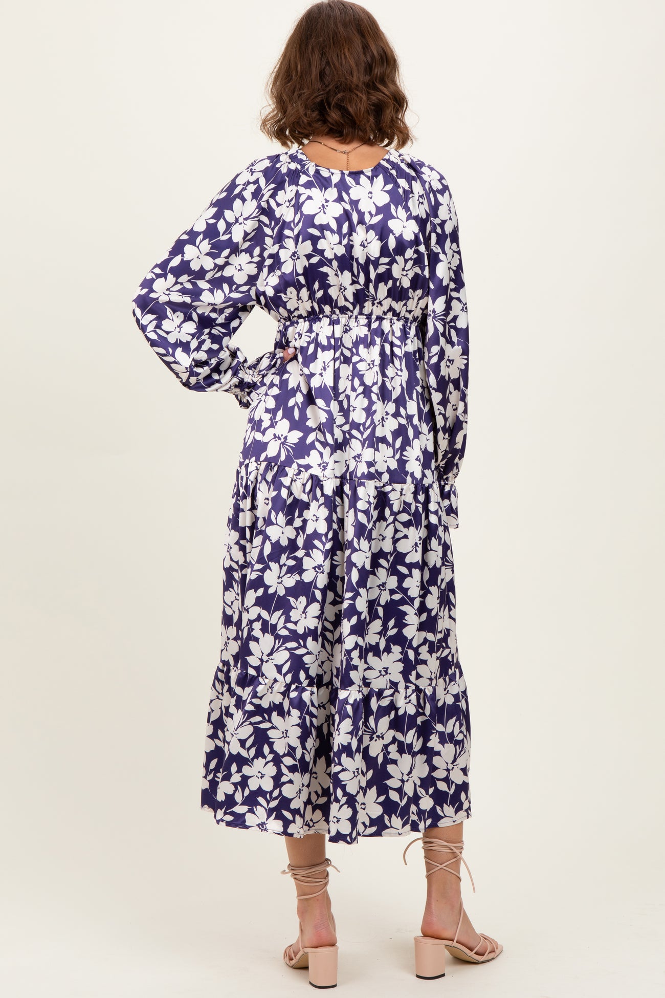 woman wearing a purple floral maxi dress with long sleeves and cinched waist, shown from the back