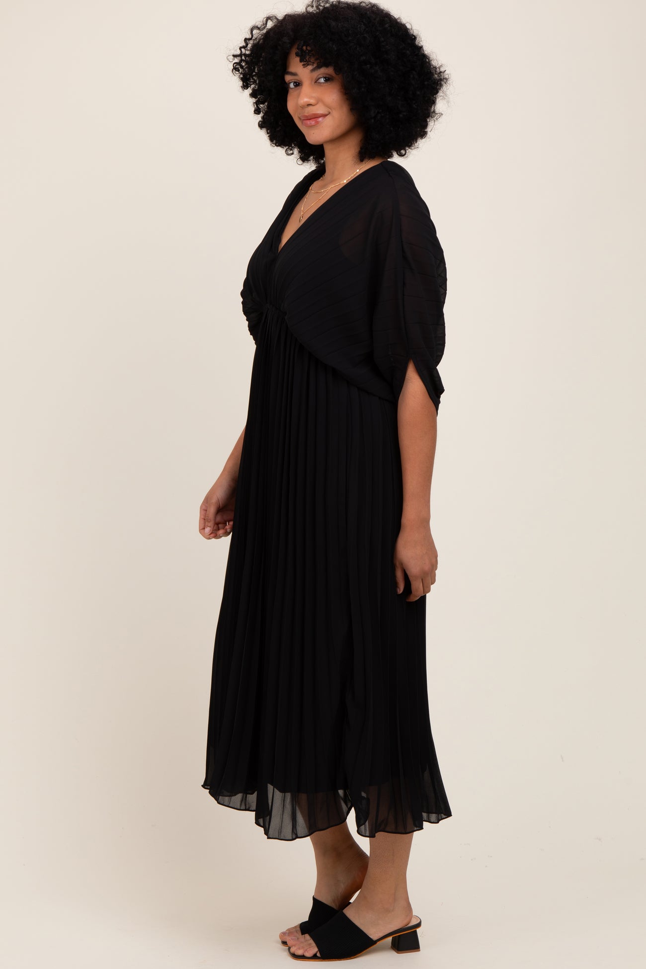 woman wearing a black pleated dress with a twisted front detail and short sleeves, styled with black sandals