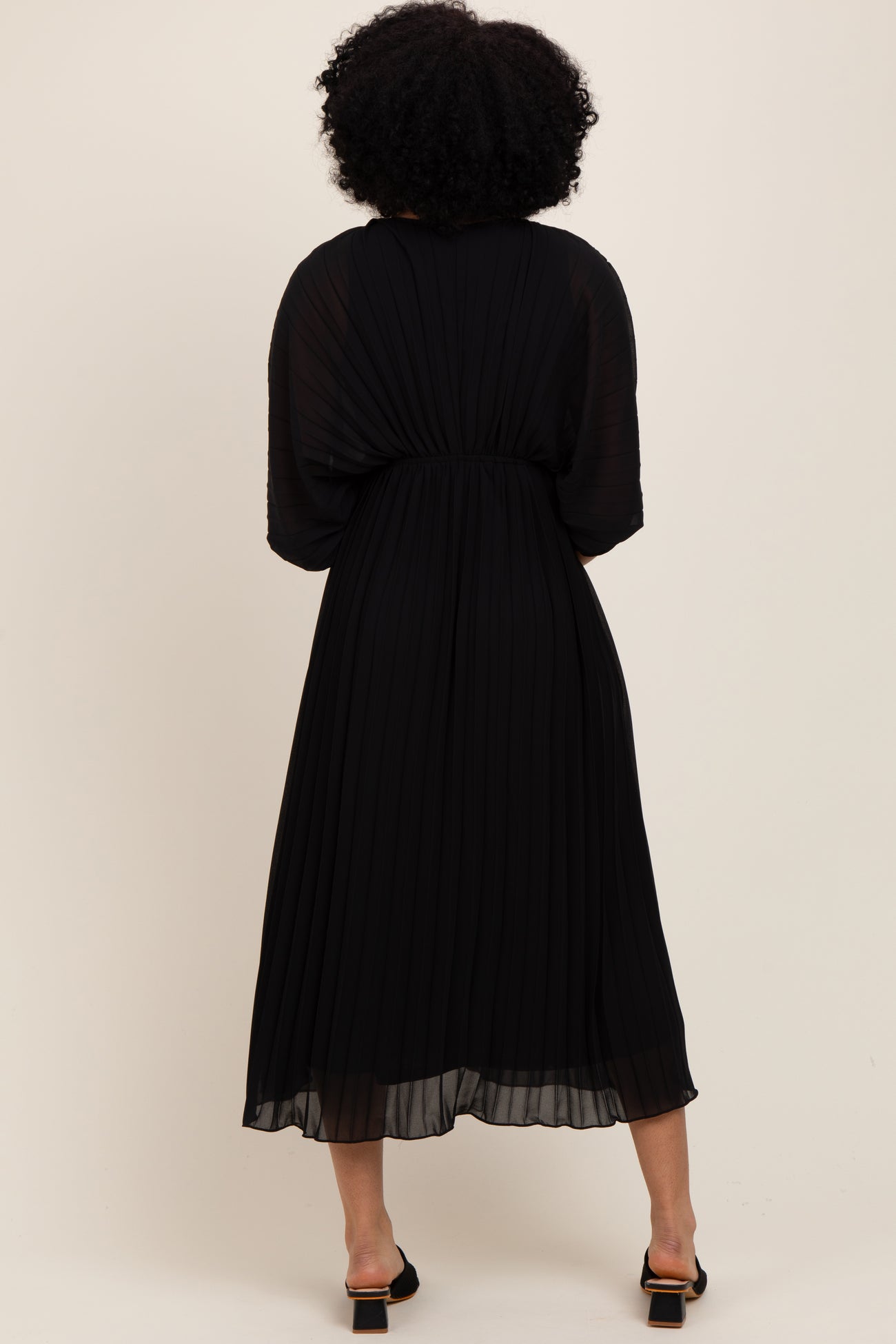 woman wearing a black pleated midi dress with a flowy silhouette and short sleeves, seen from the back