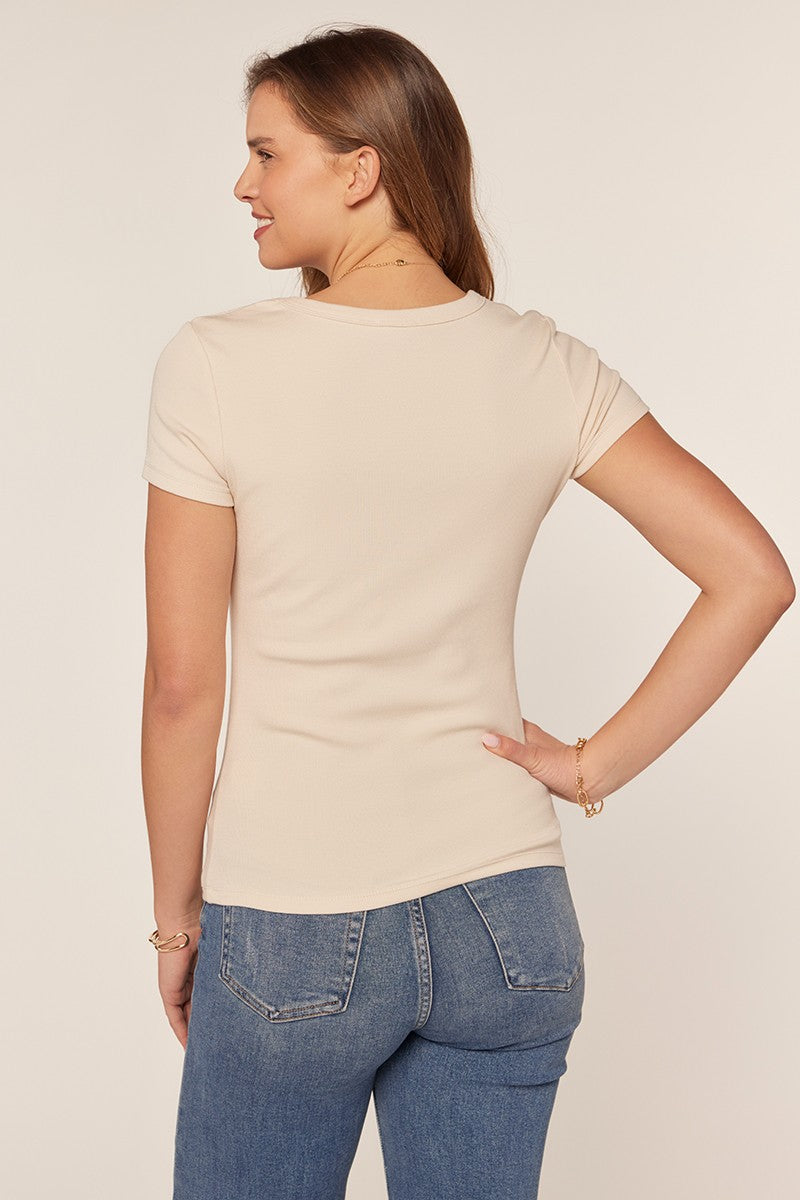 woman wearing a fitted beige short sleeve top, viewed from the back, paired with blue jeans