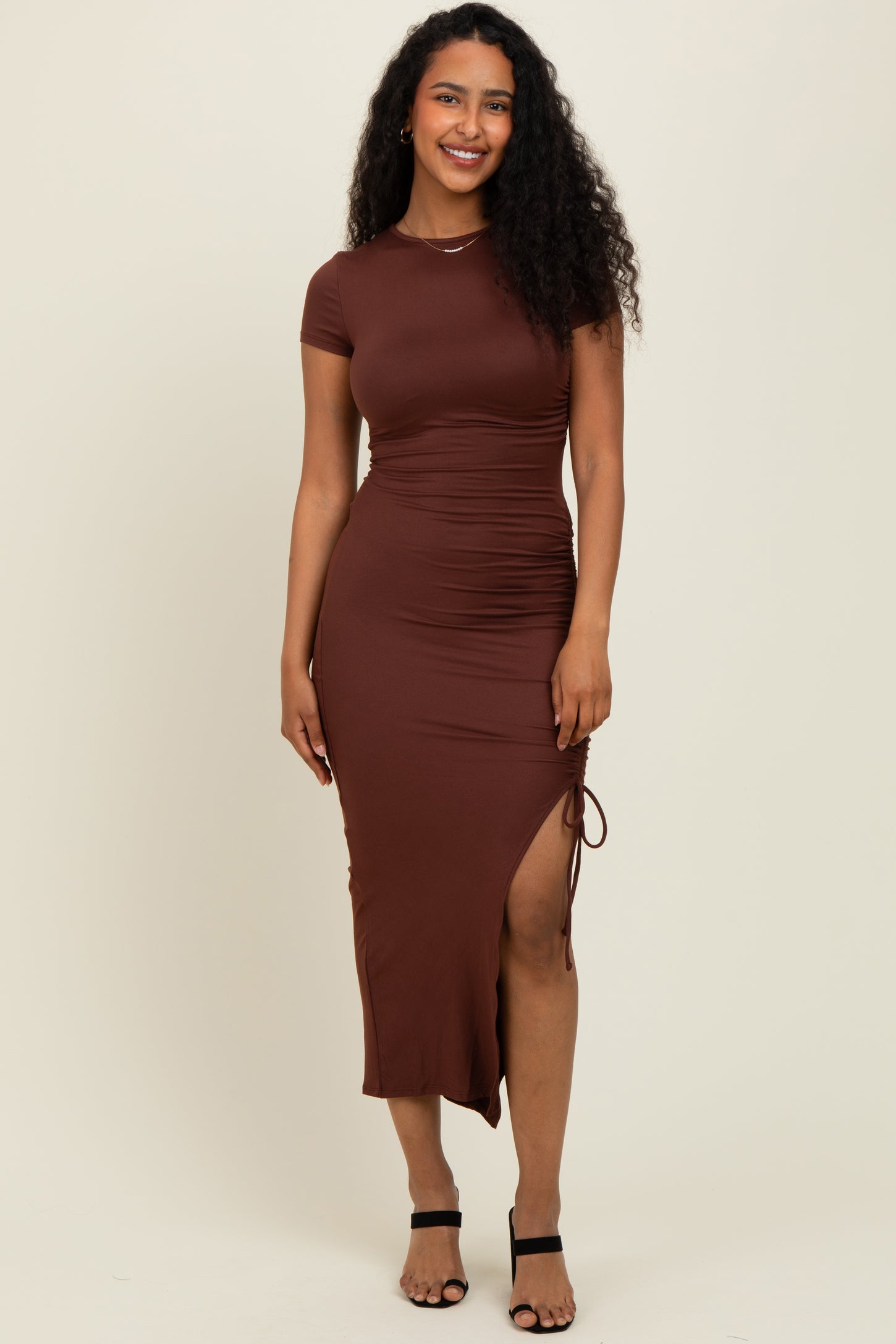 woman wearing a brown bodycon dress with short sleeves and a side slit, styled with black strappy heels