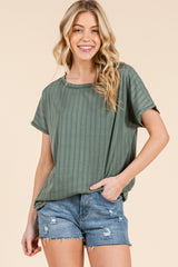 woman wearing an olive green ribbed short sleeve top paired with distressed denim shorts, smiling at the camera