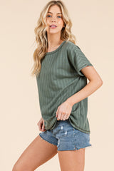 woman wearing a green ribbed short sleeve top with rolled sleeves and distressed denim shorts