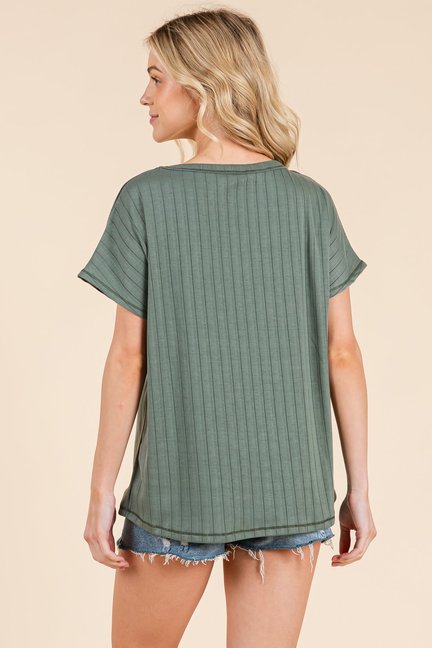 woman wearing a green ribbed short sleeve top with a relaxed fit and a rounded hem, paired with denim shorts