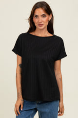 woman wearing a black short sleeve ribbed top with a relaxed fit, standing in front of a neutral background