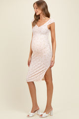 woman wearing a light pink floral maternity dress with a fitted silhouette and side slit, showing her baby bump