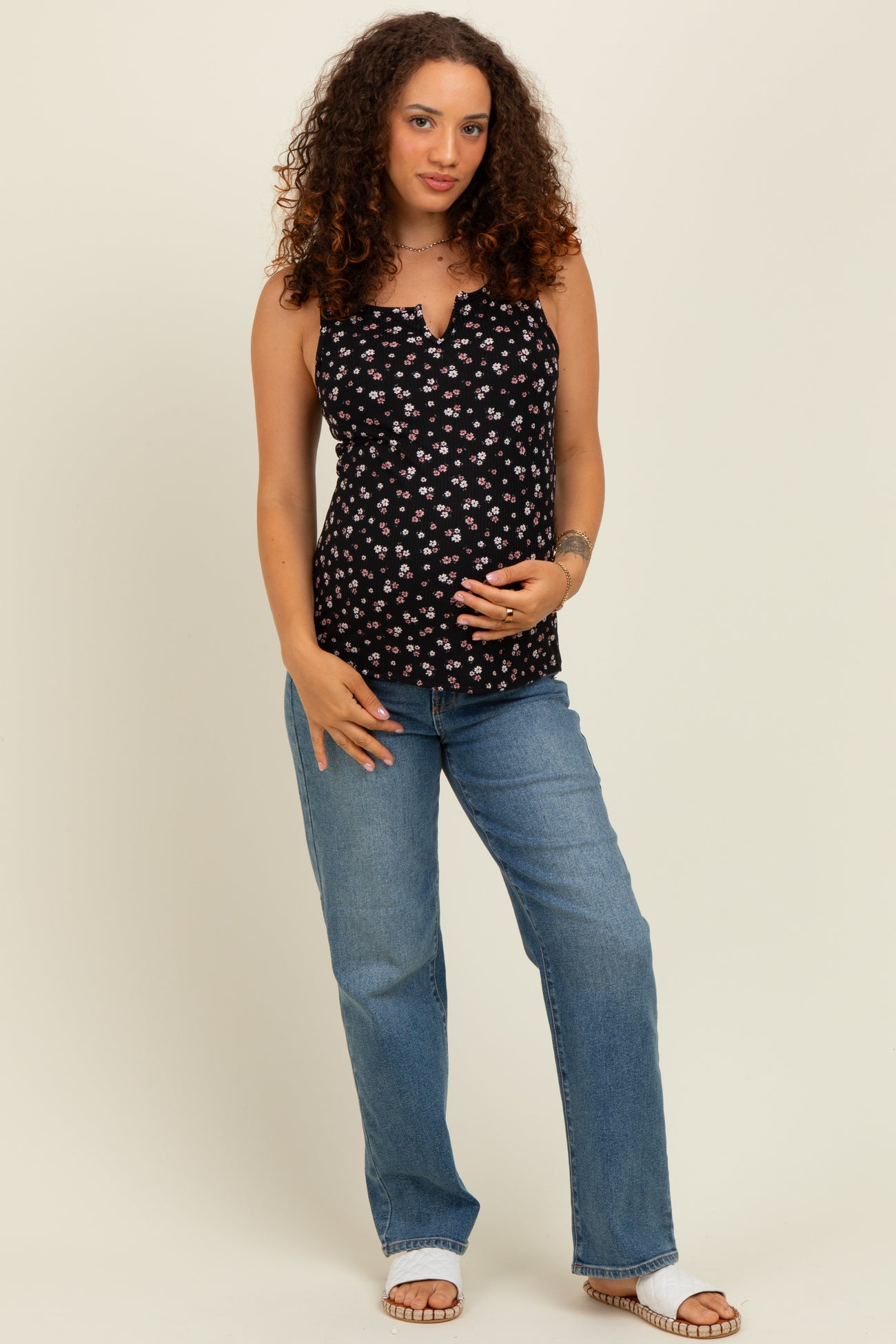 woman wearing a black floral maternity tank top and blue jeans, holding her baby bump