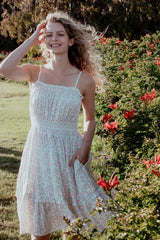 woman wearing a white floral sundress with thin straps and a tiered hem, posing in a garden with red flowers