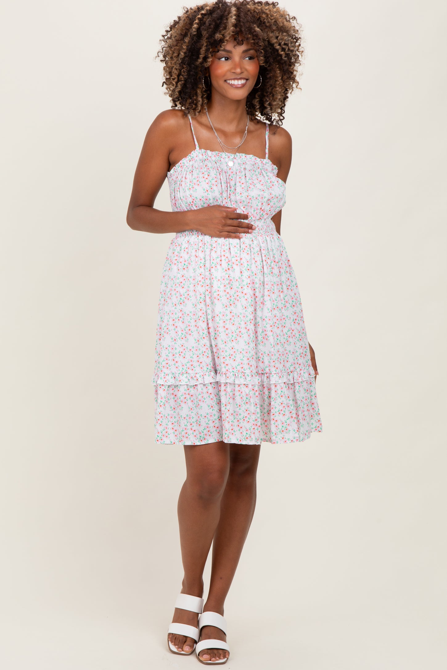 woman wearing a floral maternity dress with spaghetti straps and a ruffled hem, holding her baby bump