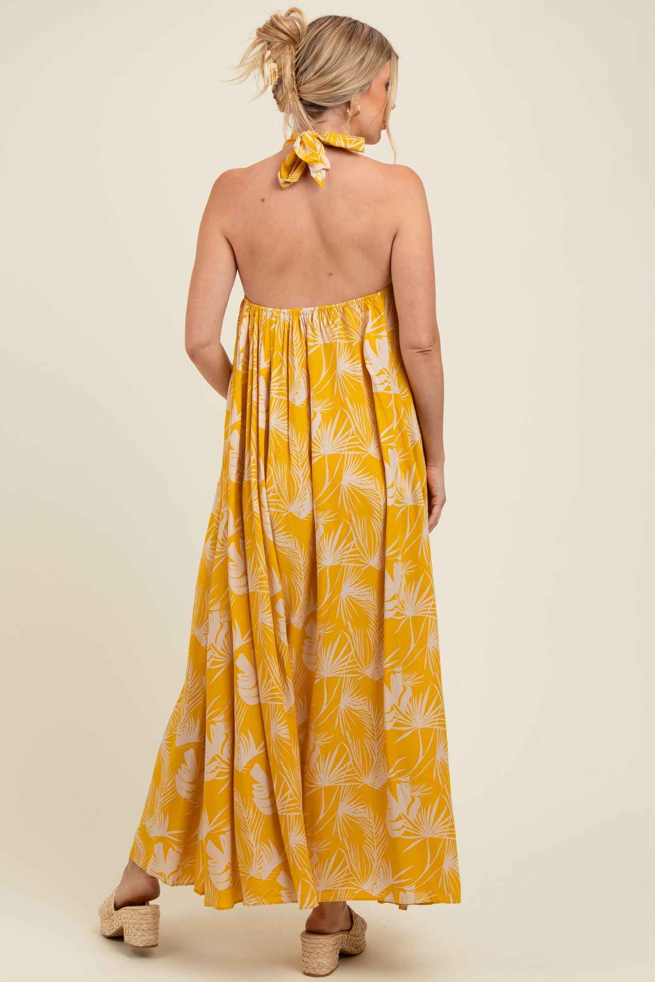 woman wearing a yellow floral print maternity maxi dress with a halter neck and open back, showing a baby bump