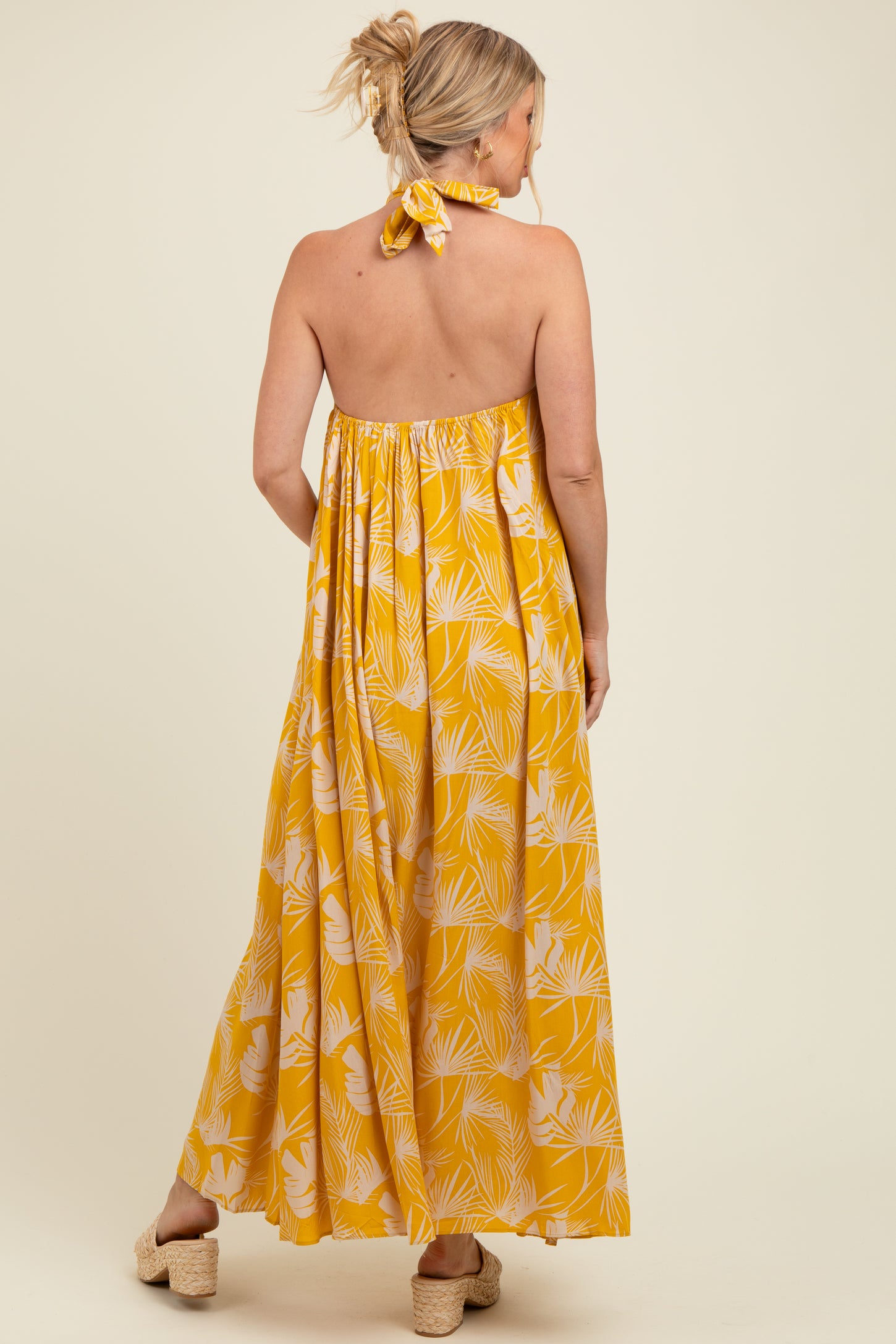 woman wearing a yellow floral print maternity maxi dress with a halter neck and open back, showing a baby bump
