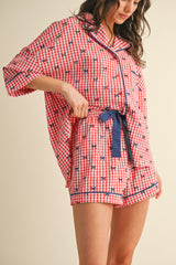 woman wearing a red and white gingham print short pajama set with navy trim and bow detail
