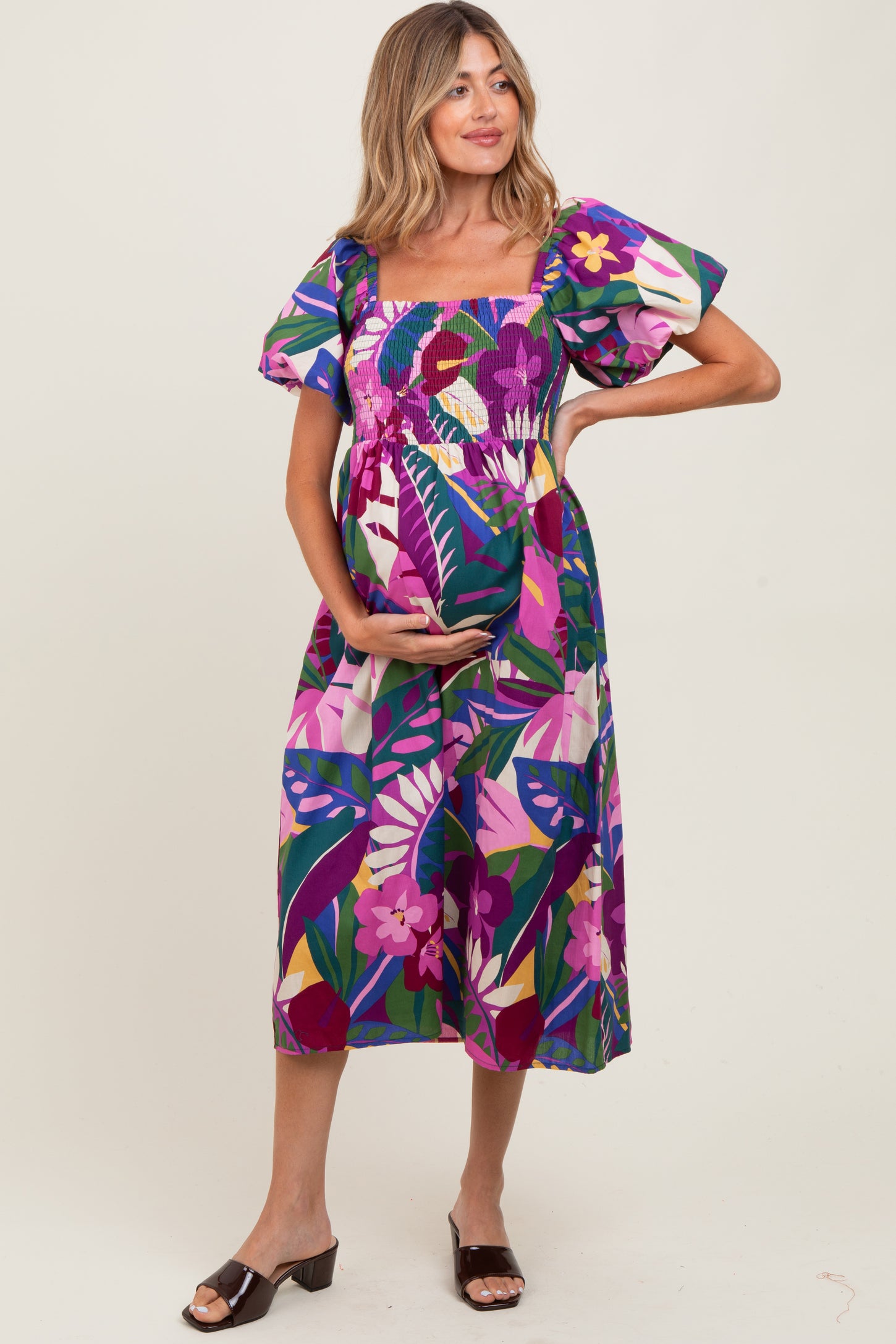 woman wearing a colorful floral print maternity dress with puff sleeves and holding her baby bump