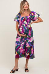 woman wearing a colorful floral print maternity dress with puff sleeves and holding her baby bump