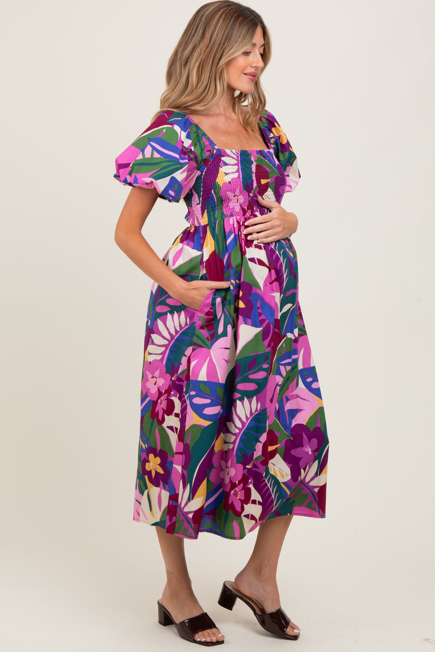 woman wearing a colorful floral print maternity dress with puff sleeves and holding her baby bump