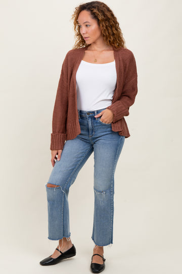 woman wearing a brown knit cardigan over a white tank top and blue high-waisted ripped jeans