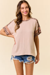woman wearing a light pink short sleeve top with leopard print accents and distressed denim shorts